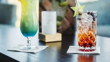 Two cocktails on a wooden table with a framed picture in the background.