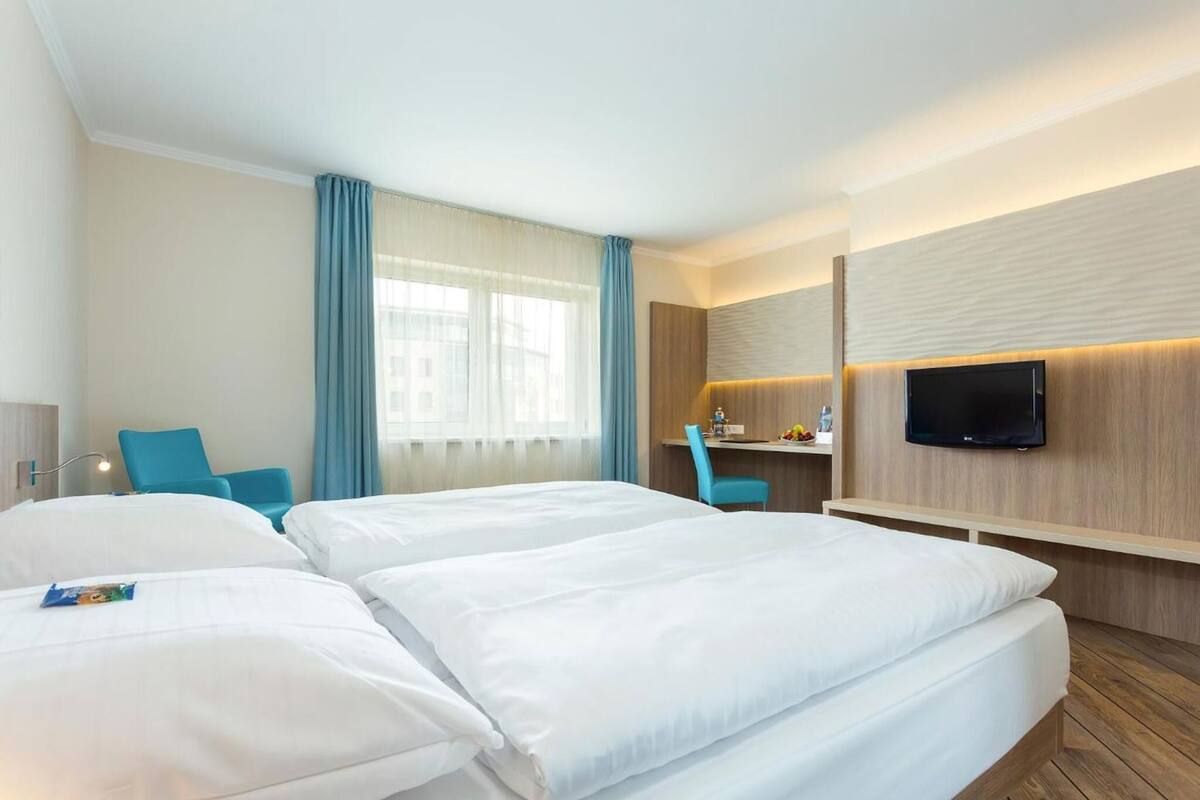 Habitación de hotel con dos camas, un escritorio, una silla, un televisor y una ventana con cortinas.