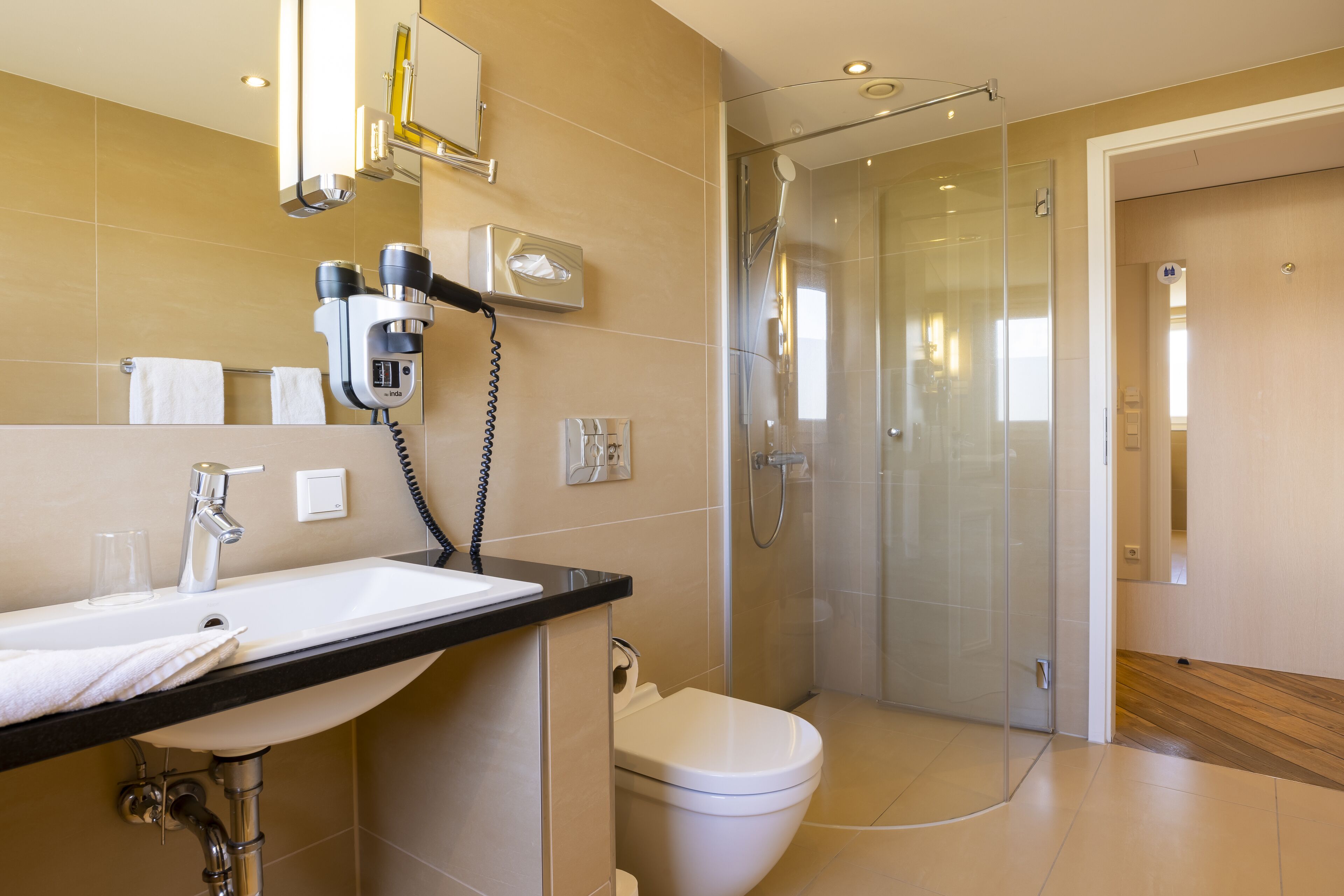 A modern bathroom with a sink, mirror, hairdryer, and shower.