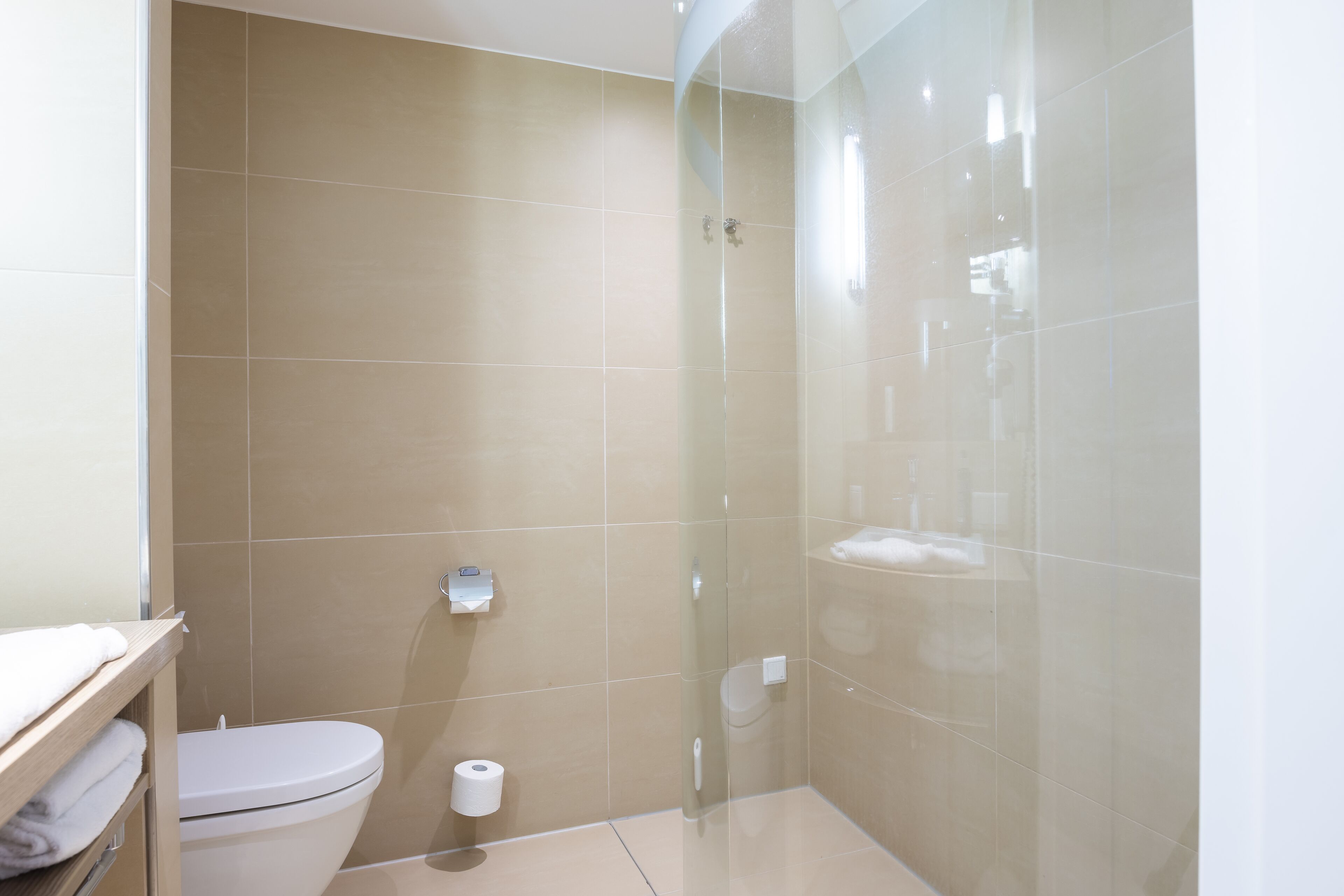 Une salle de bain avec des toilettes, une douche en verre et des carreaux de couleur beige.