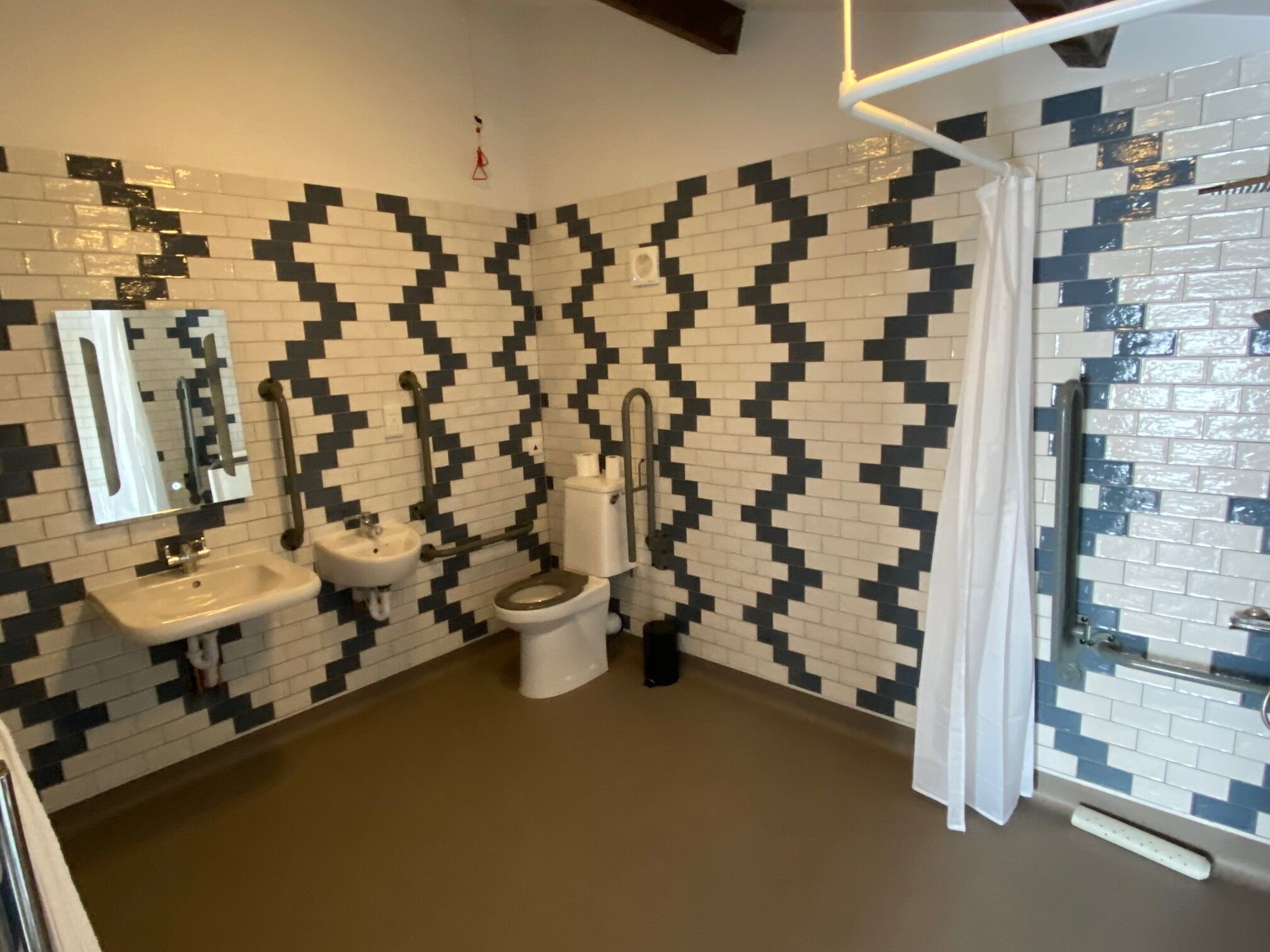 A bathroom with a black and white patterned tile wall, a sink, a toilet, and a shower area.