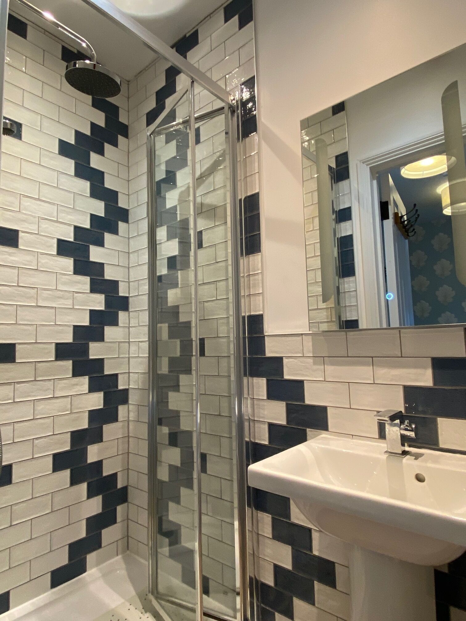 Un baño con cabina de ducha de vidrio, un lavabo blanco y una pared de azulejos con diseño blanco y negro.