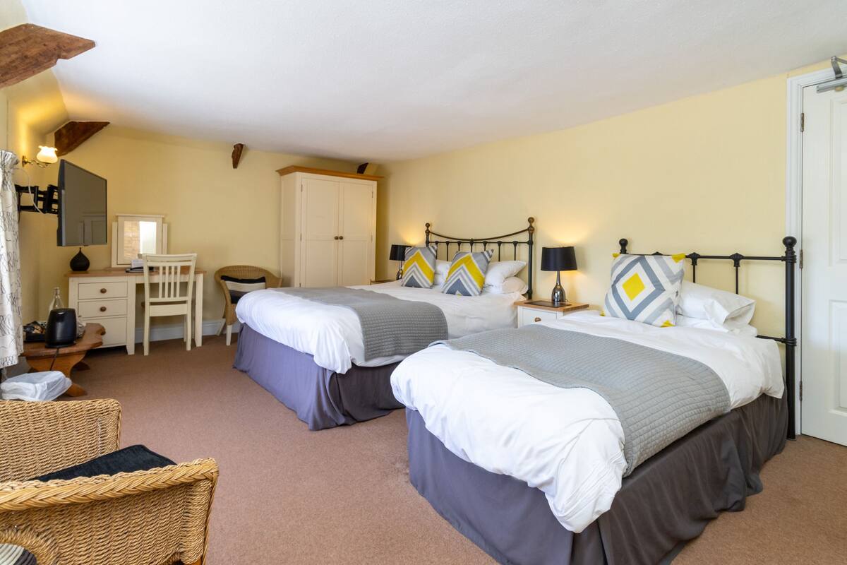 Quarto de hotel com duas camas, uma escrivaninha, uma cadeira e um guarda-roupa.