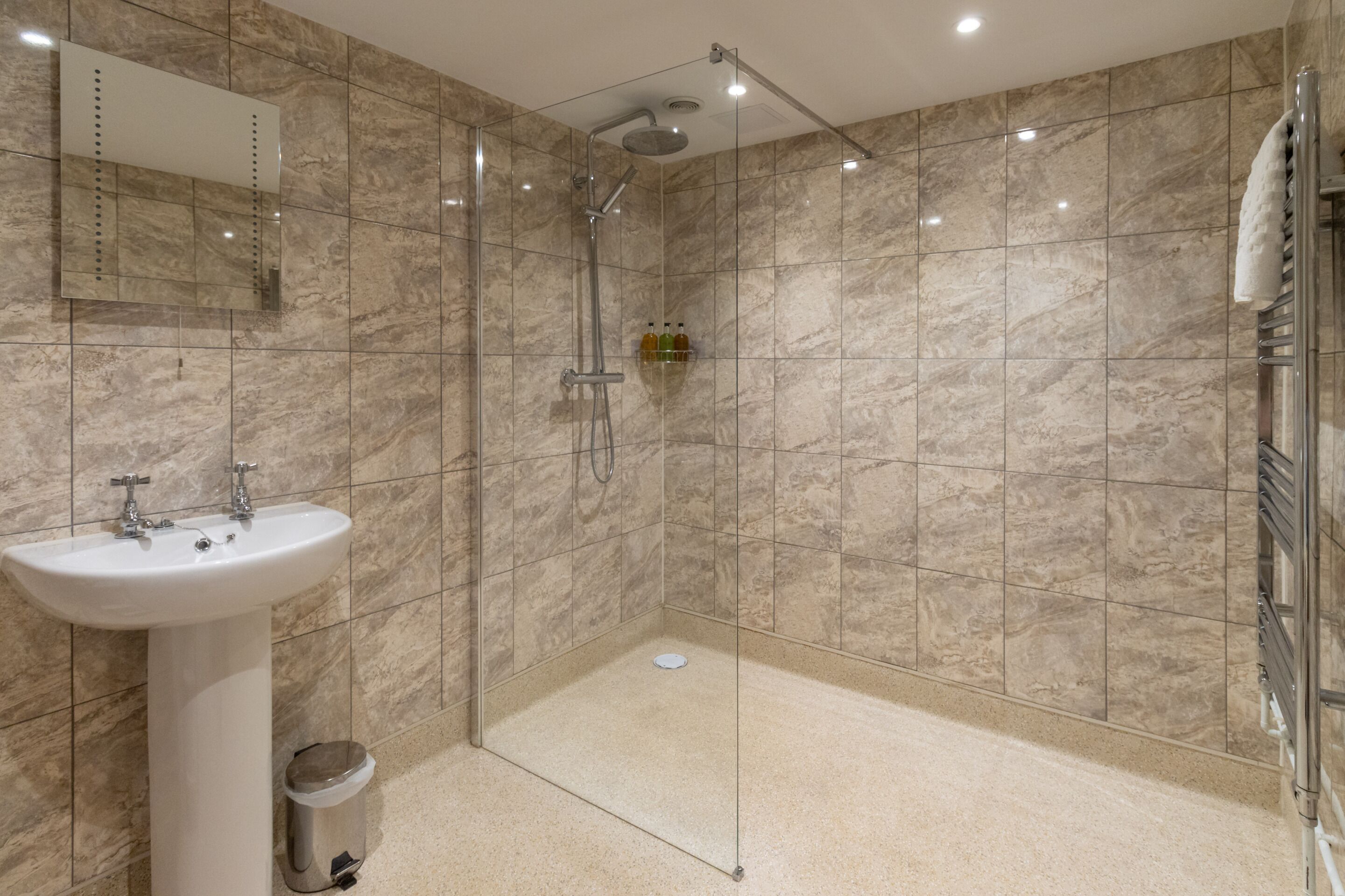 A modern bathroom with a glass-enclosed shower, a pedestal sink, and a mirror.