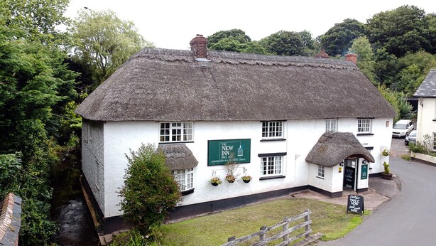 A traditional thatched-roof inn with a sign indicating it has been a hotel since 1830.