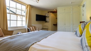A bedroom with a large bed, a television mounted on the wall, a radiator, and a wardrobe. - The New Inn (Crediton)