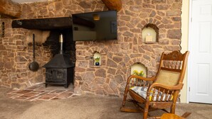 A stone fireplace with a TV mounted above it, a wooden rocking chair, and a small shelf with decorative items. - The New Inn (Crediton)