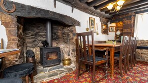 A rustic room with a stone fireplace, wooden furniture, and a colorful carpet. - The New Inn (Crediton)