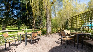 An outdoor seating area with wooden tables and chairs, surrounded by trees and a wooden fence.