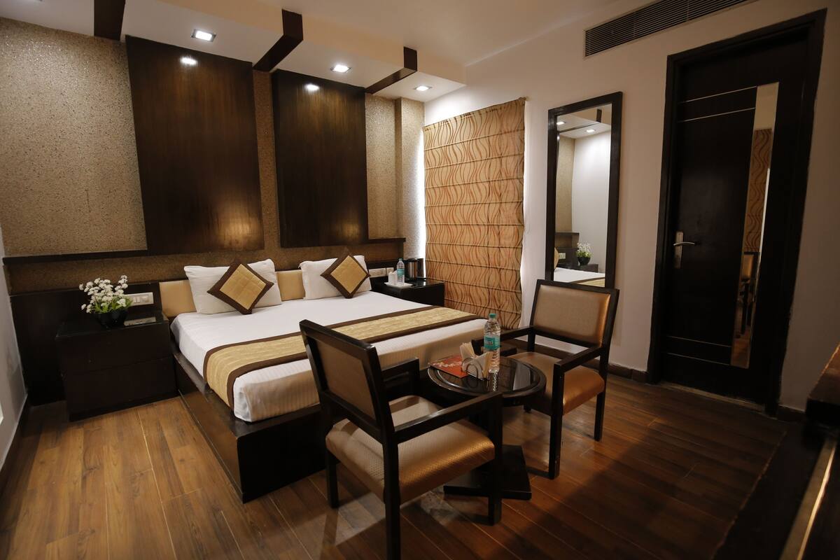 A hotel room with a large bed, a bedside table, a chair, a small table, and a mirror.