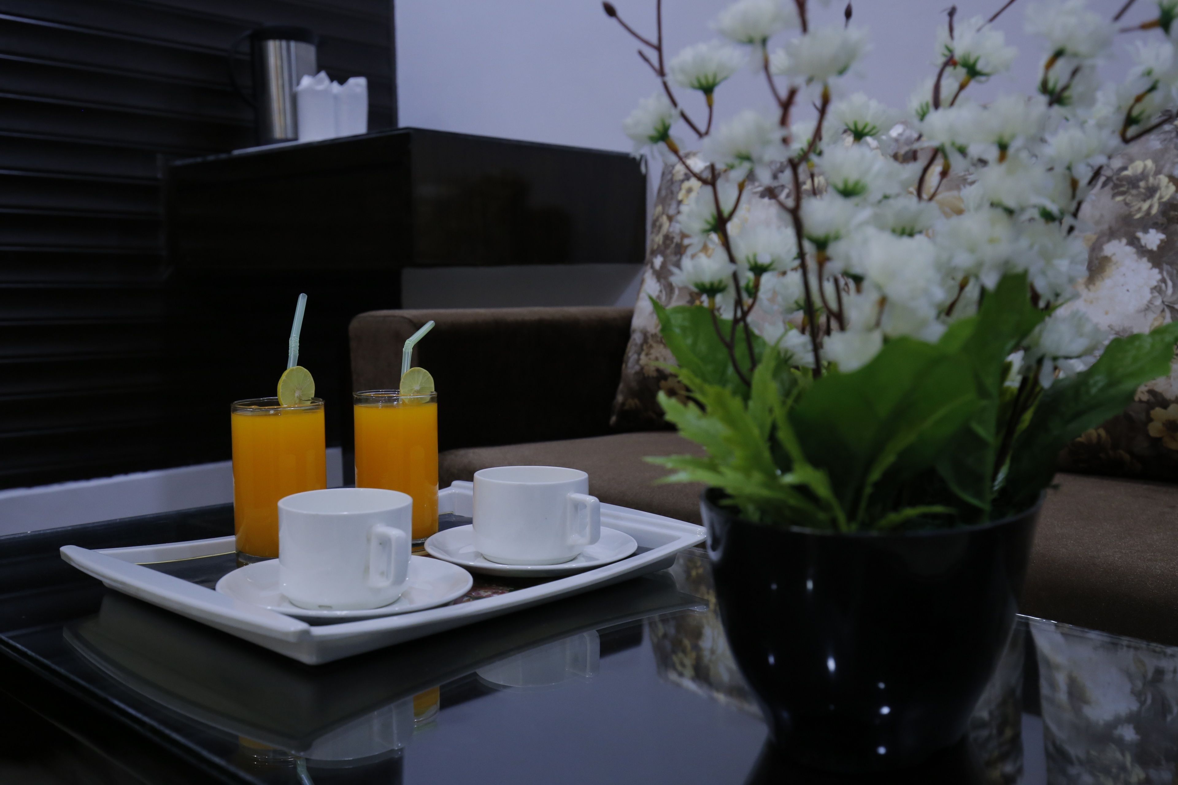 Una bandeja con dos tazas blancas y dos vasos de jugo de naranja sobre una mesa.