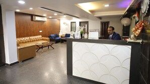 A reception area with a brown leather sofa, a blue couch, and a reception desk with a decorative panel. - Hotel Delhi Pride (New Delhi)