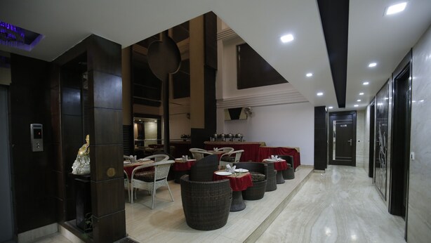 A modern hotel lobby with a marble floor, dark wooden columns, and a seating area with wicker chairs and tables. - Hotel Delhi Pride (New Delhi)
