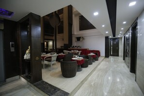 A modern hotel lobby with a marble floor, dark wooden columns, and a seating area with wicker chairs and tables. - Hotel Delhi Pride (New Delhi)