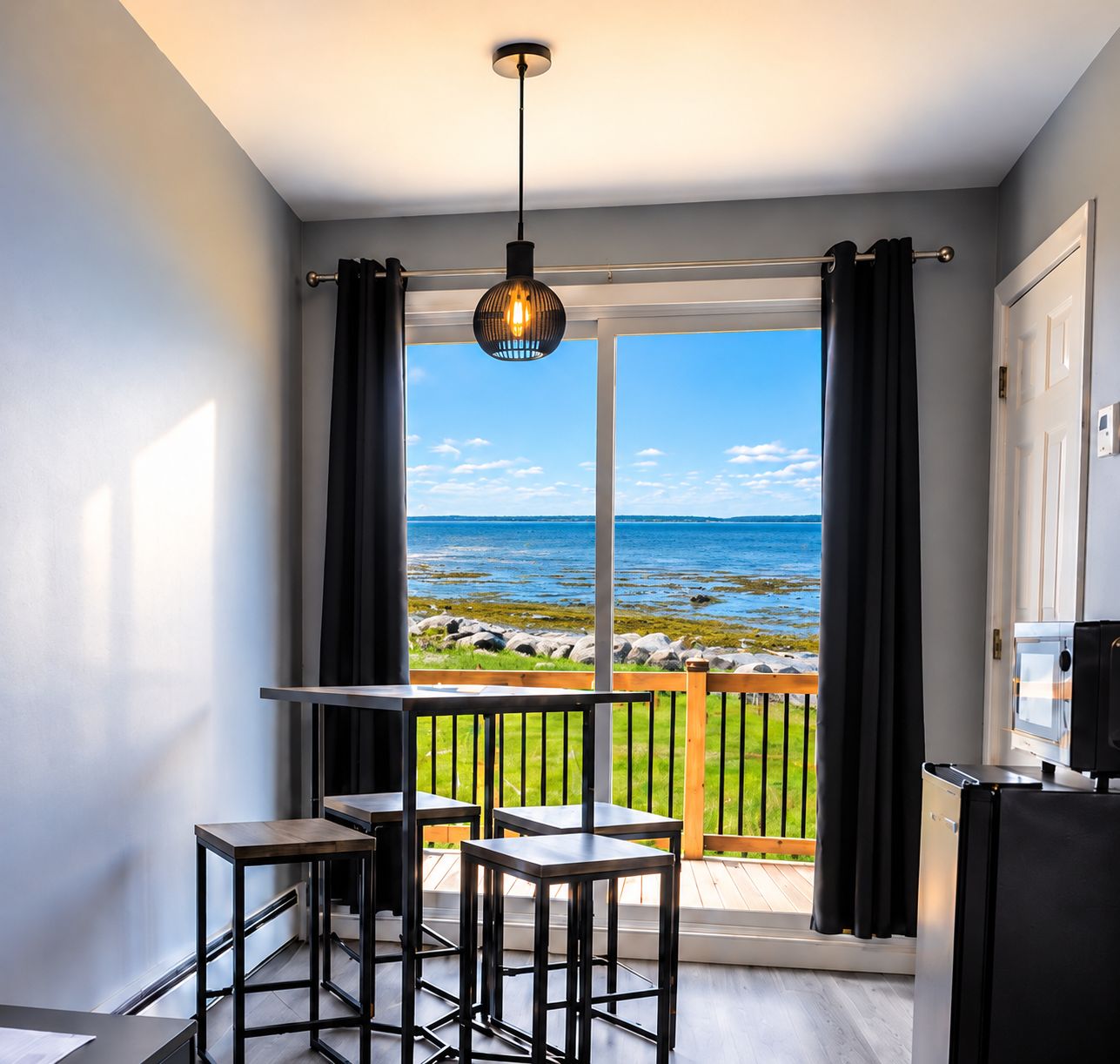 Un balcon avec vue sur la mer, un luminaire suspendu et une petite table avec des chaises.
