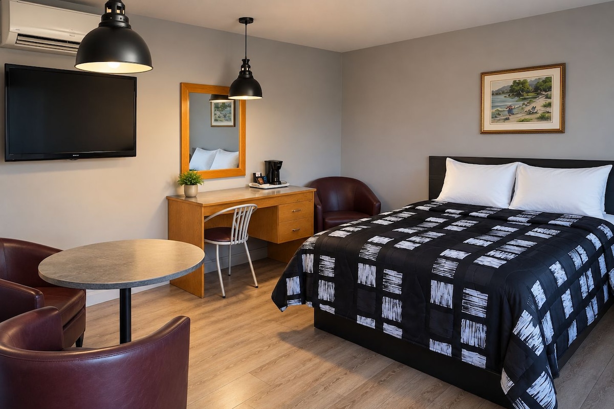 A hotel room with a bed, a desk, a chair, a round table, a TV, and a painting on the wall.