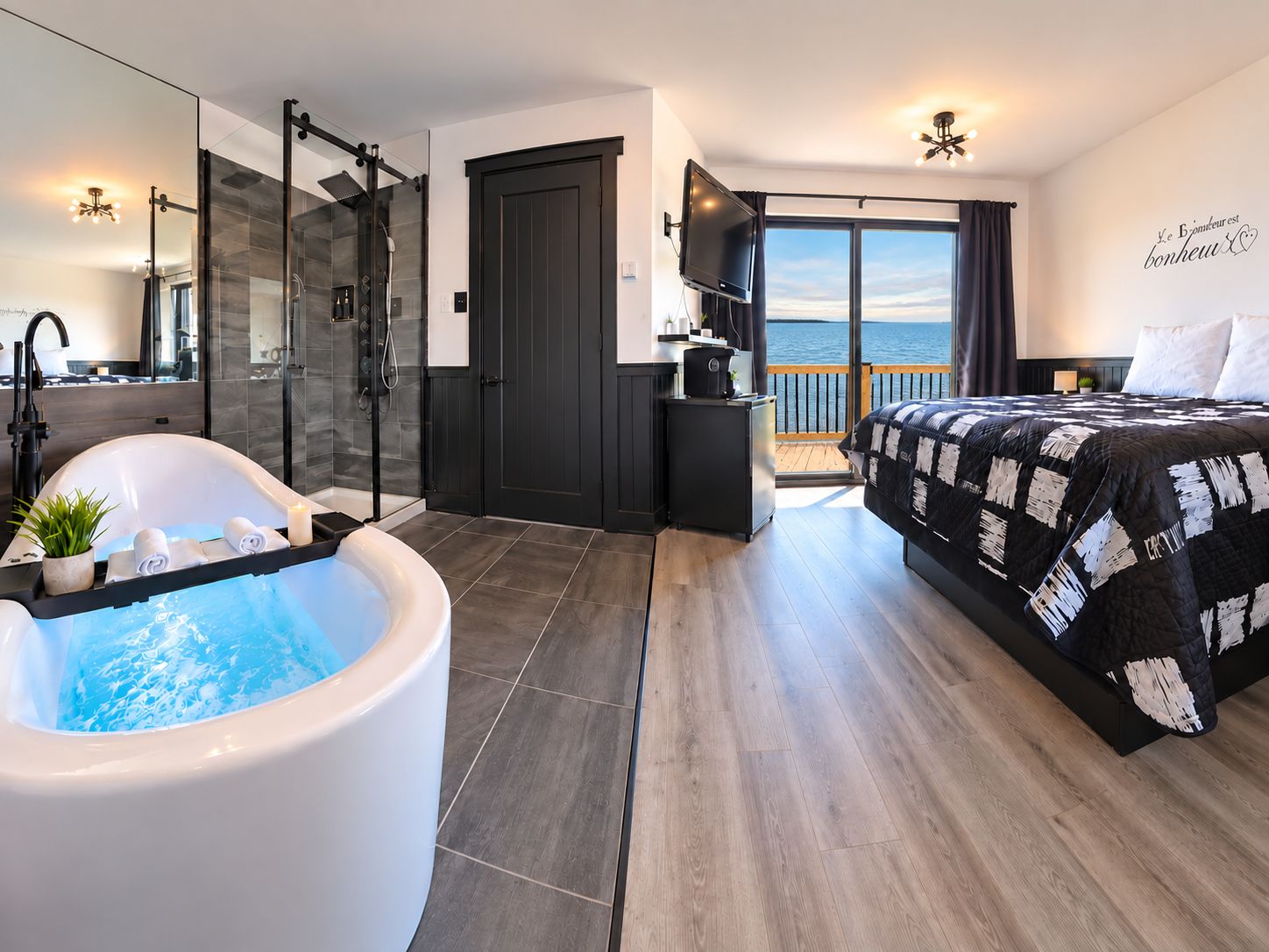 Une chambre moderne dotée d’un grand lit, d’une baignoire, d’une douche et d’un balcon offrant une vue sur la mer.