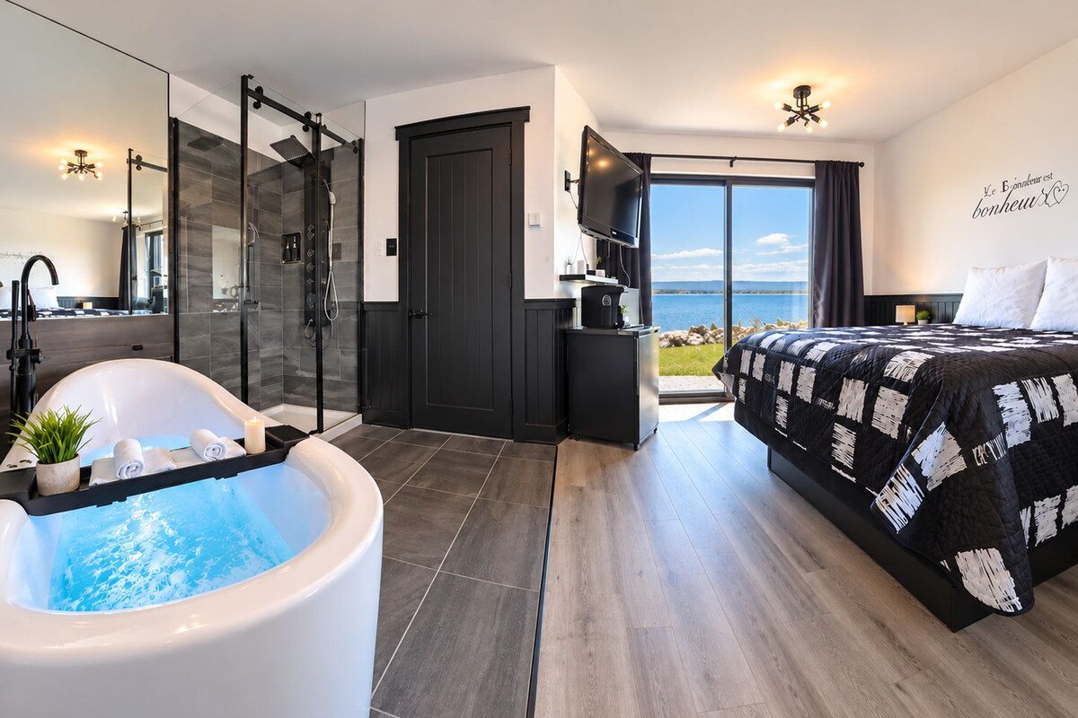 A modern bedroom with a large bed, a bathtub, a shower, and a balcony with a view.
