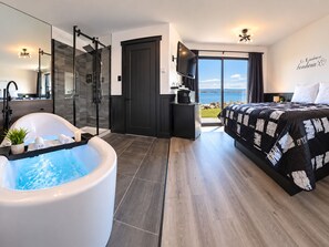 A modern bedroom with a large bed, a bathtub, a shower, and a balcony with a view. - Motel Rimouski (Rimouski)