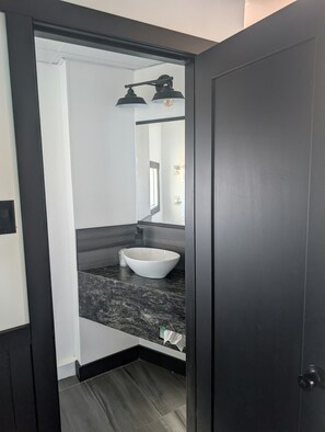 A bathroom with a white sink, dark countertop, and a mirror above it. - Motel Rimouski (Rimouski)