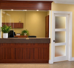 Egy fa borítással ellátott recepciós pult, egy virágtartóban lévő növény és egy matt üveglapokkal ellátott ajtó.