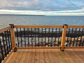 A wooden deck with a metal railing overlooking a rocky shoreline and calm sea. - Motel Rimouski (Rimouski)