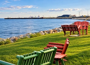 A grassy area with red Adirondack chairs and a view of the water with a ship in the distance.