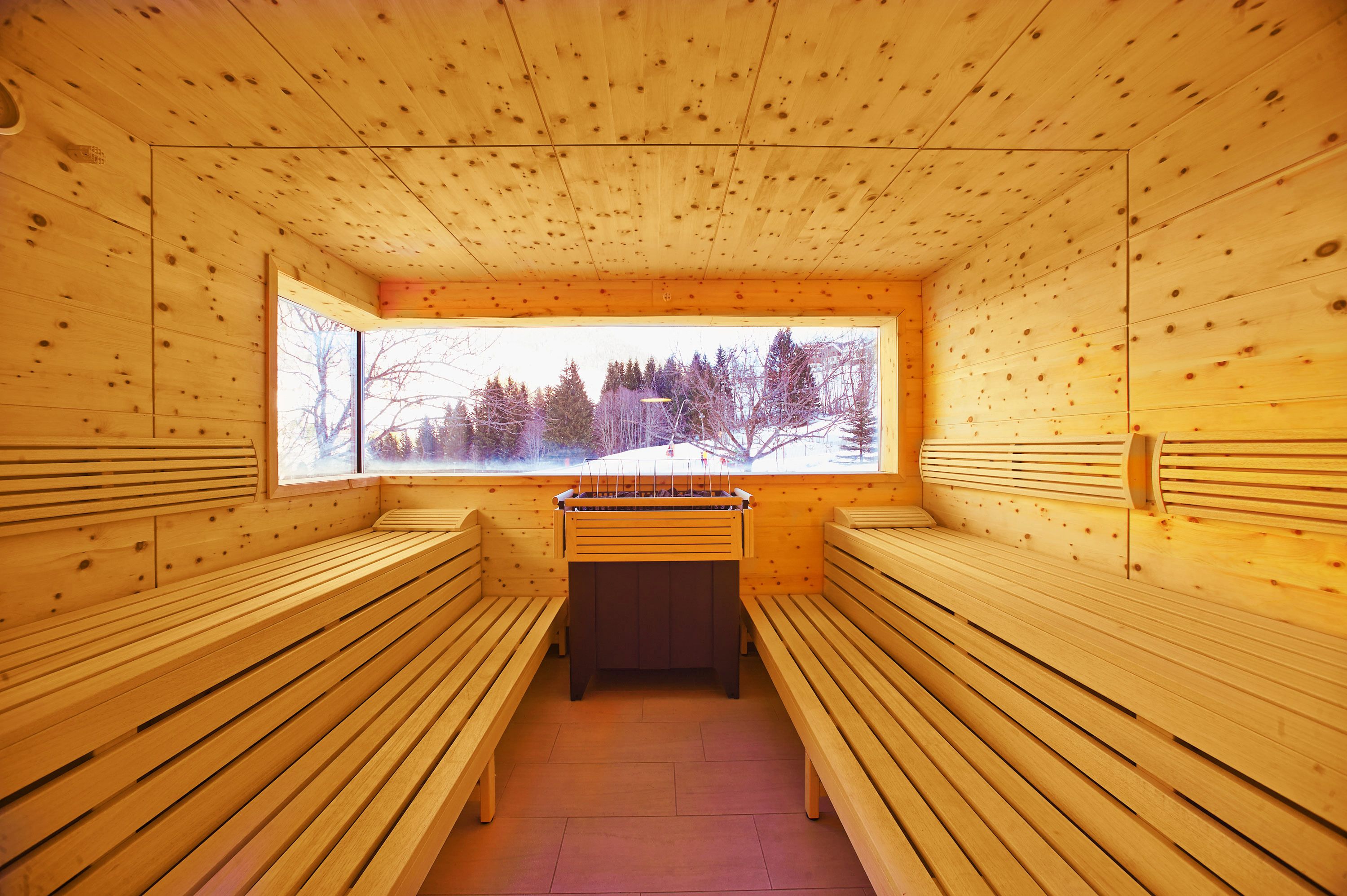 Una stanza sauna con panche in legno e un tavolo sauna, ampie finestre con vista sugli alberi.