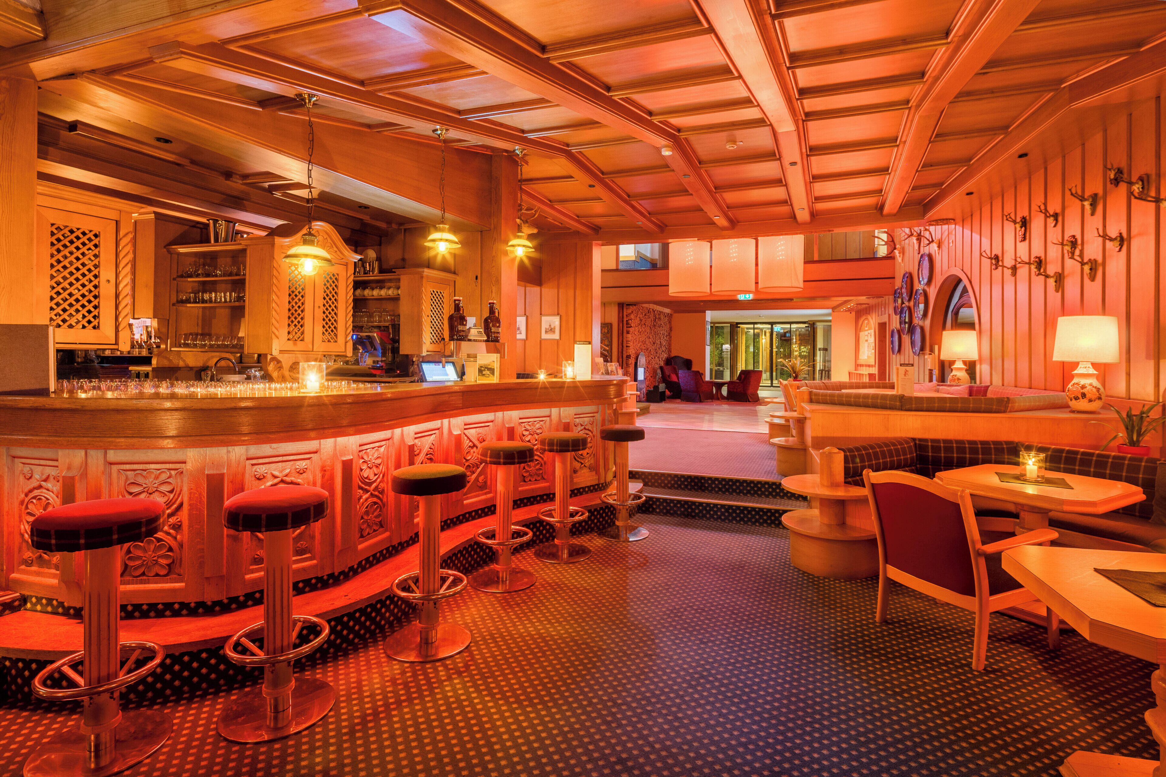 Una zona de bar con taburetes, una barra y un área de asientos con mesas y sillas.