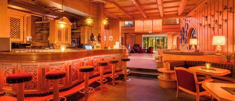 Una zona de bar con taburetes, una barra y un área de asientos con mesas y sillas.