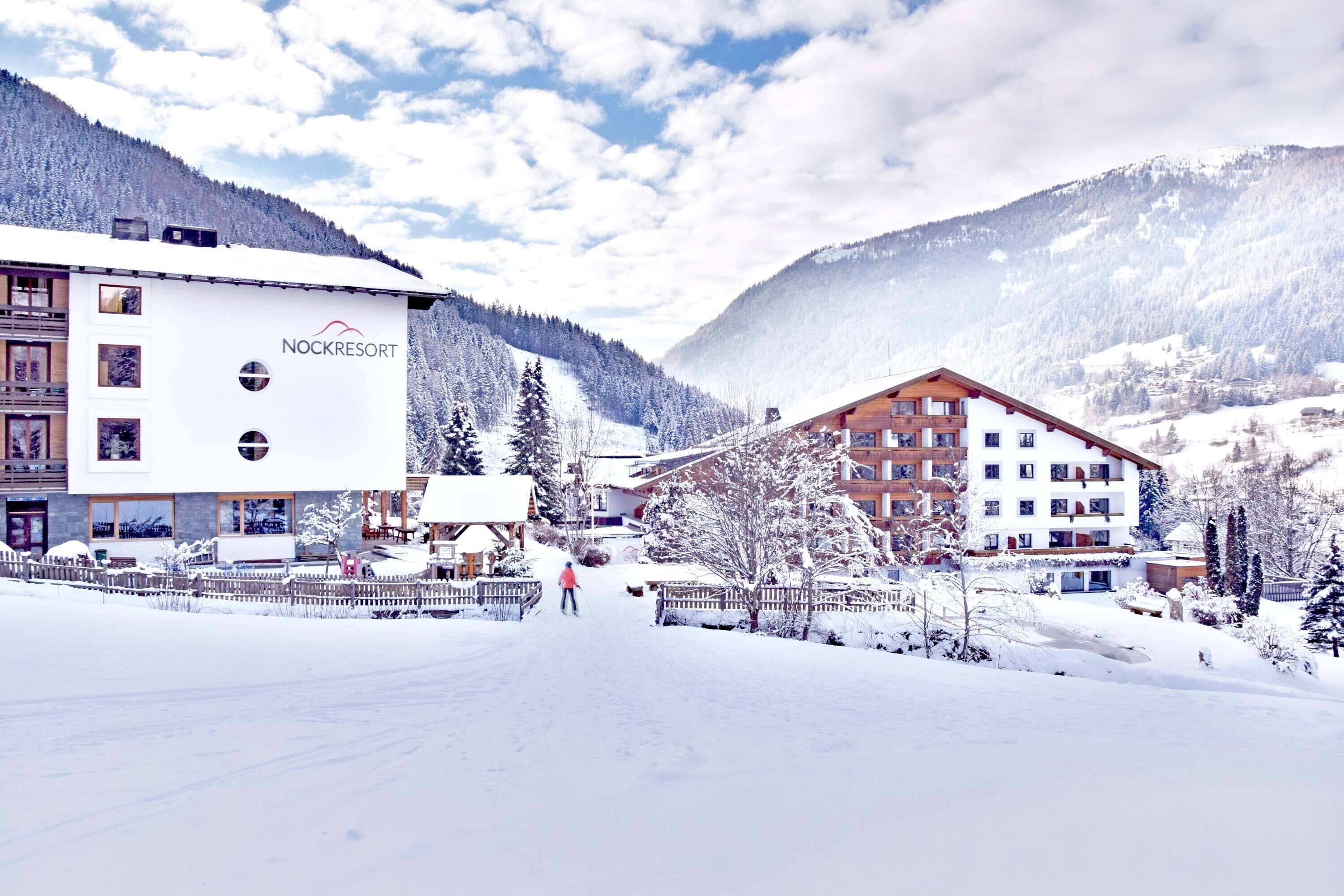 A snow-covered resort with buildings, including a lodge with a ski slope and a mountain backdrop.