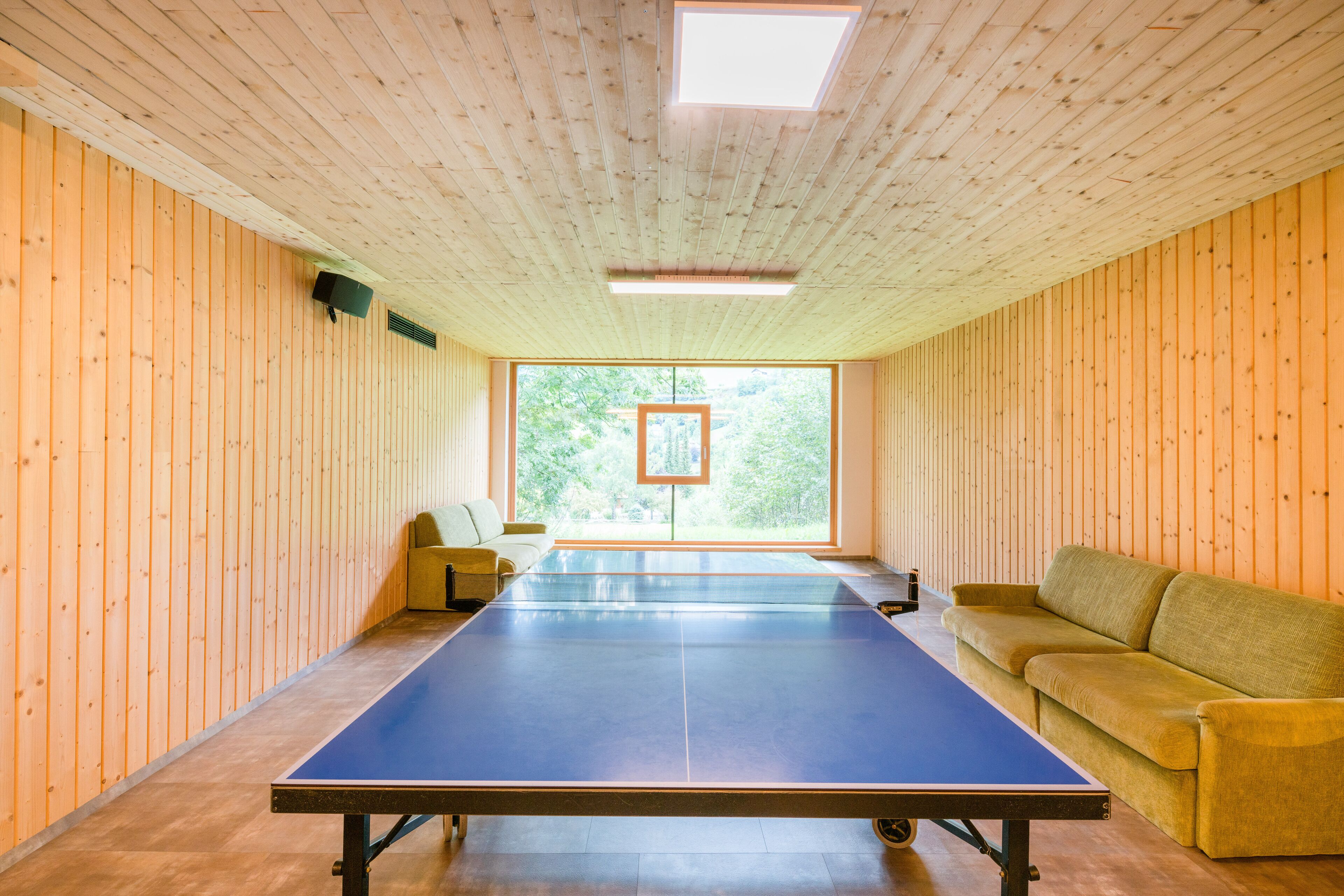 Una habitación con mesa de ping pong, sofá y ventana con vista a zonas verdes.