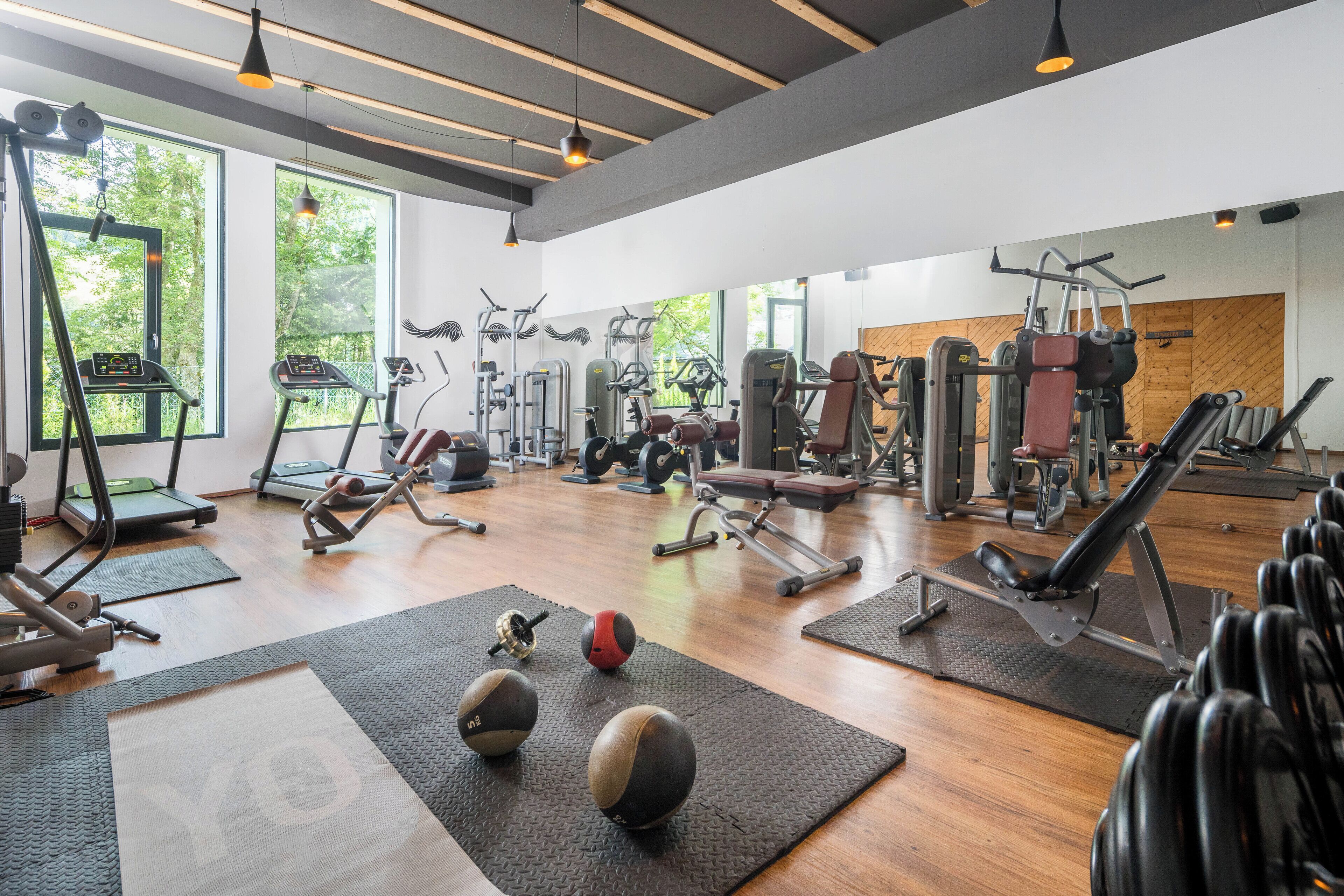 A gym with various exercise equipment, large windows, and a wooden floor.