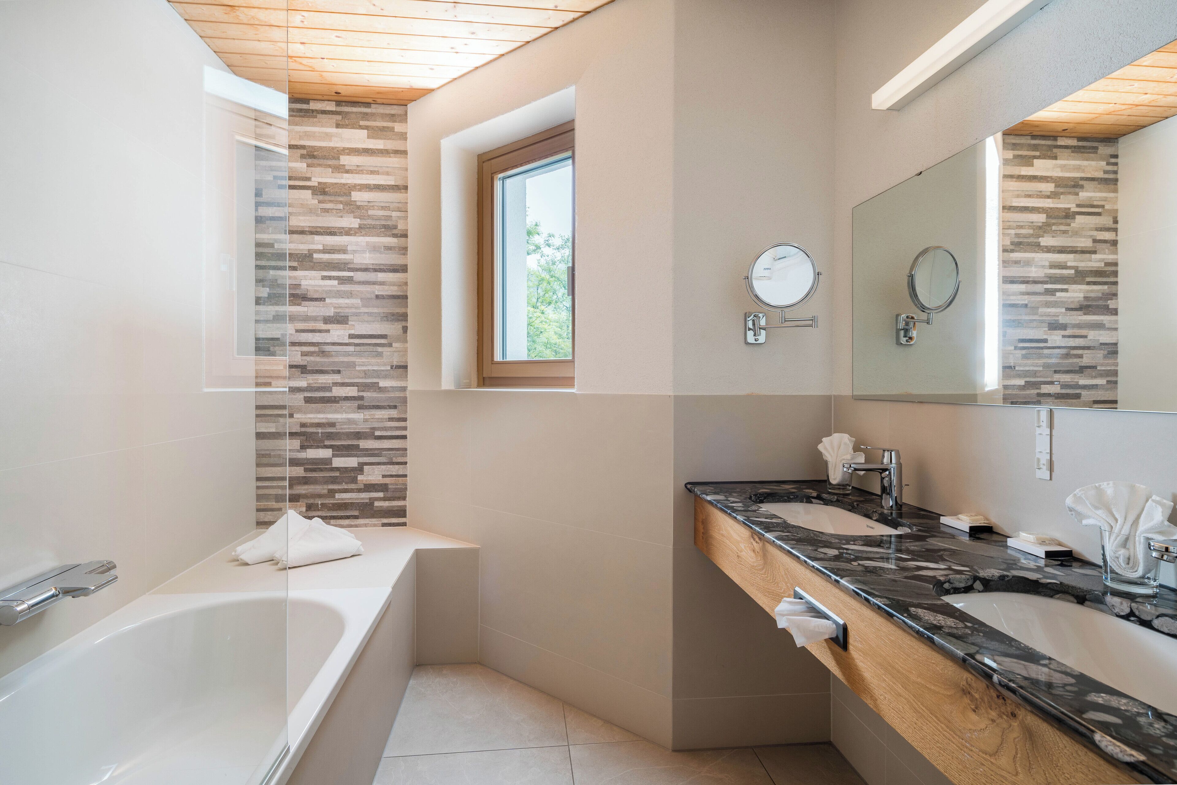 Un baño moderno con bañera, dos lavamanos y un espejo grande.
