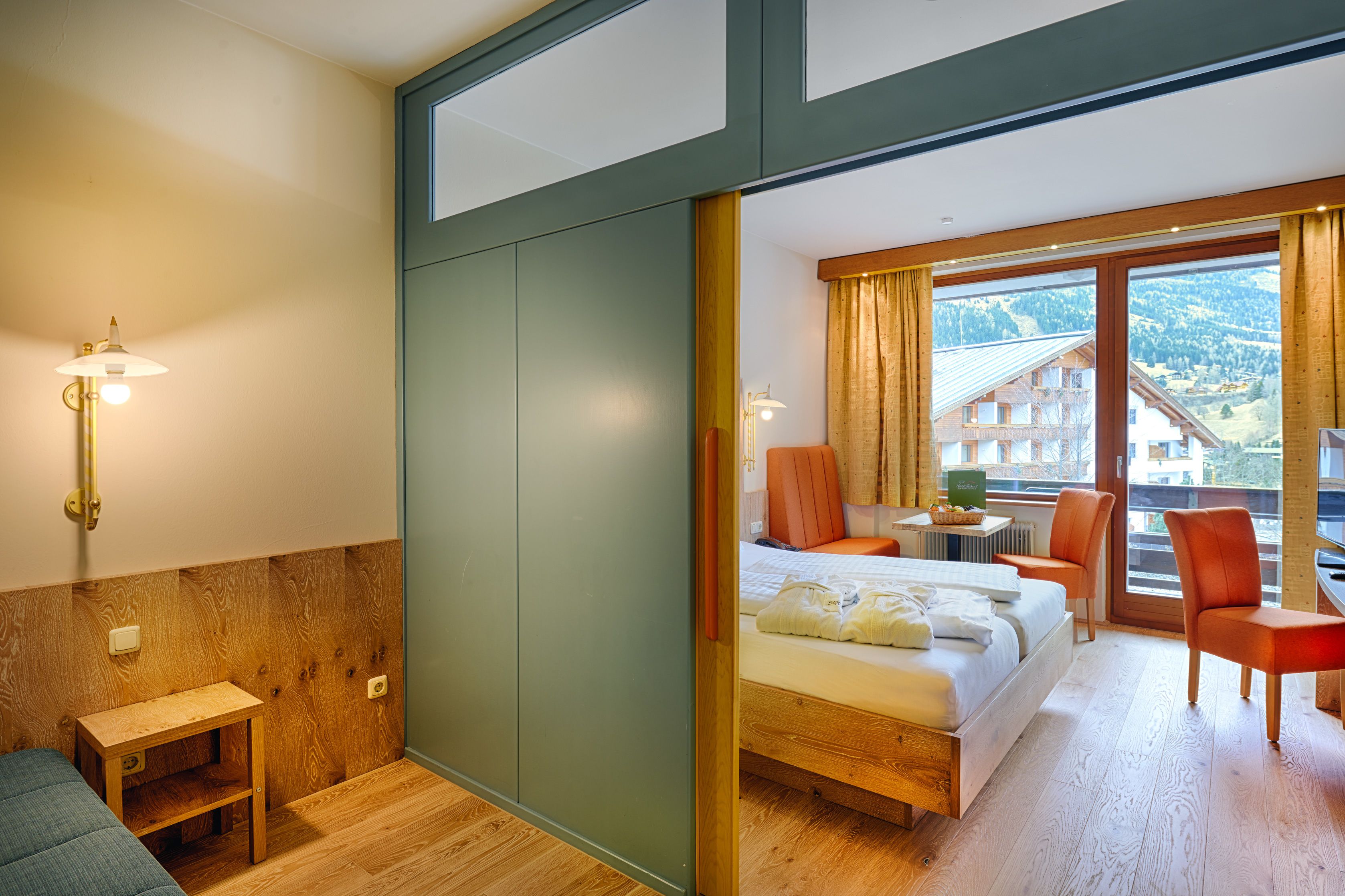 A hotel room with a bed, a small table, a chair, and a view of a mountain and buildings.