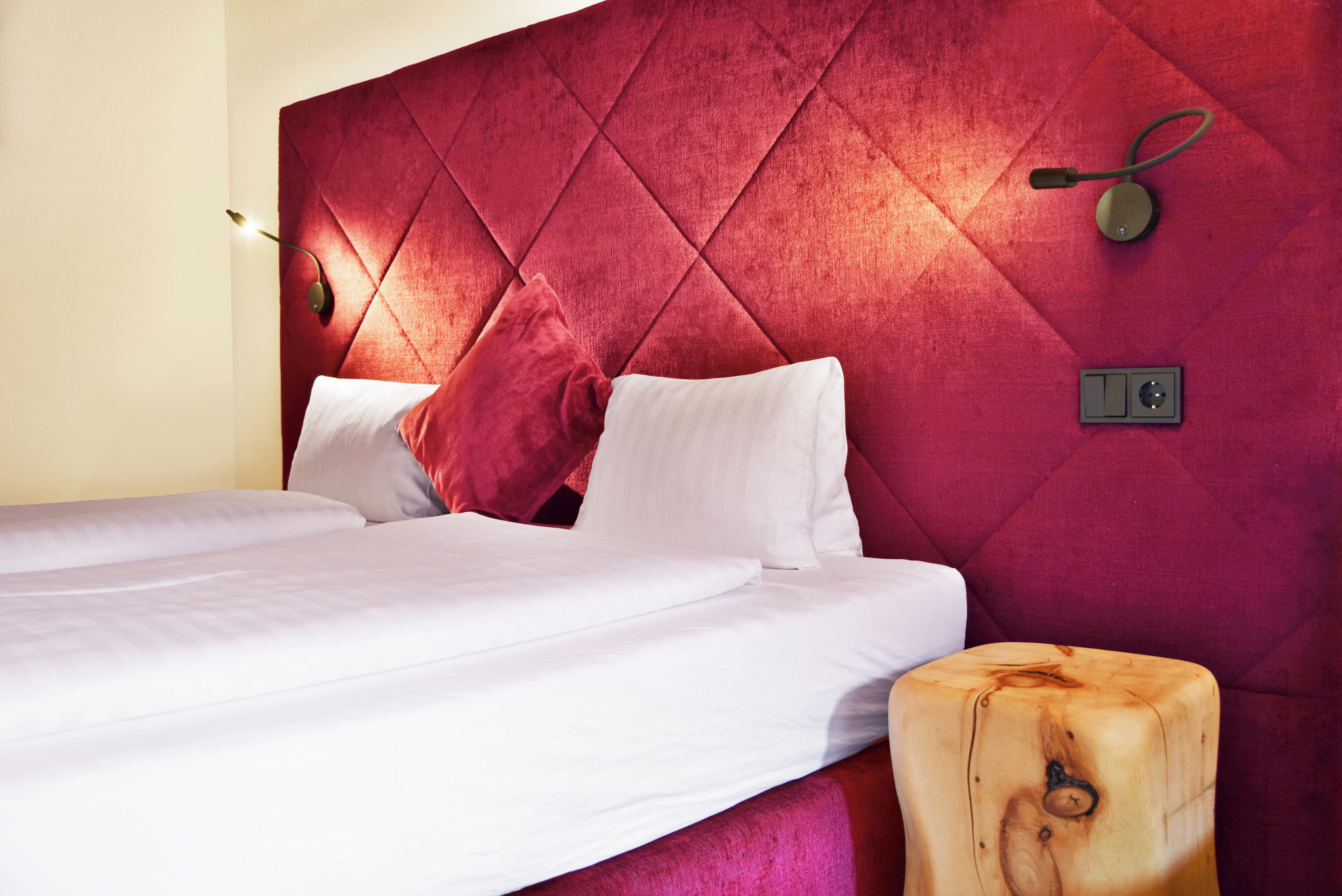 A bed with white linens, a red upholstered headboard, and a wooden nightstand.
