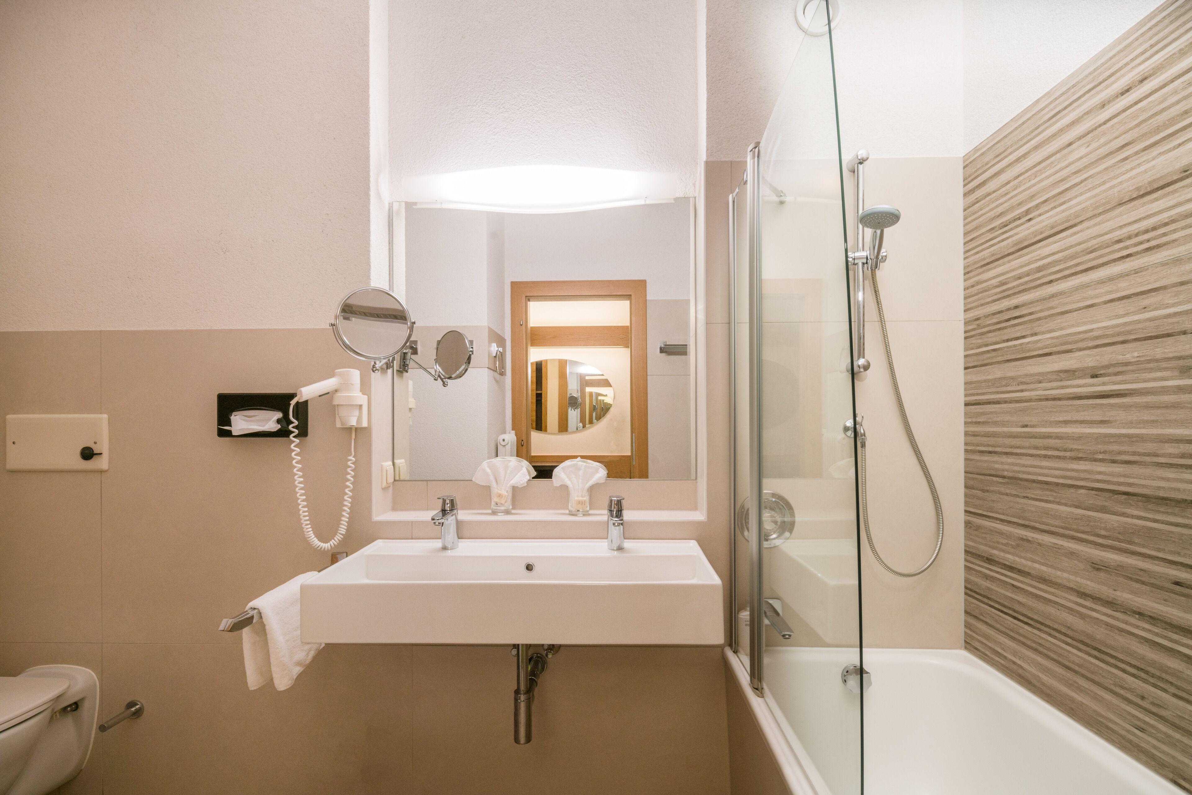 A modern bathroom with a sink, mirrors, a handheld showerhead, and a glass-enclosed shower.