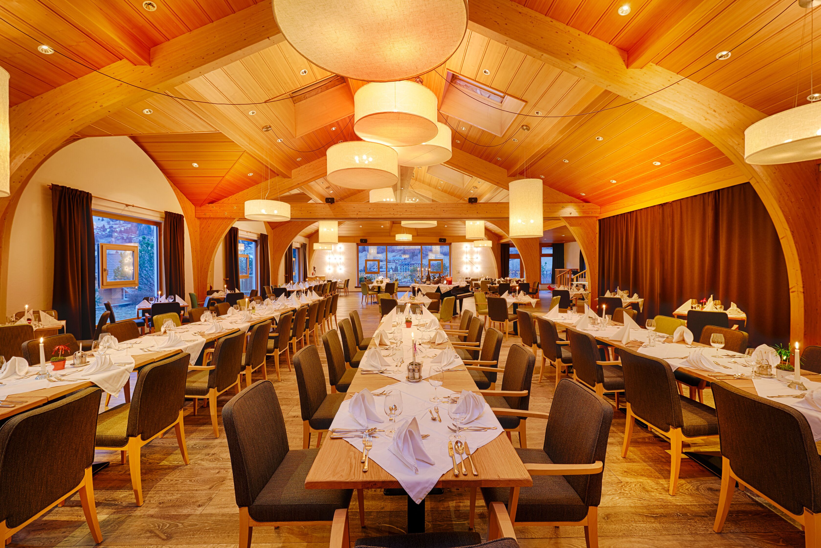Ein großer Festsaal mit langen Tischen, Holzbalkendecke und großen Fenstern.