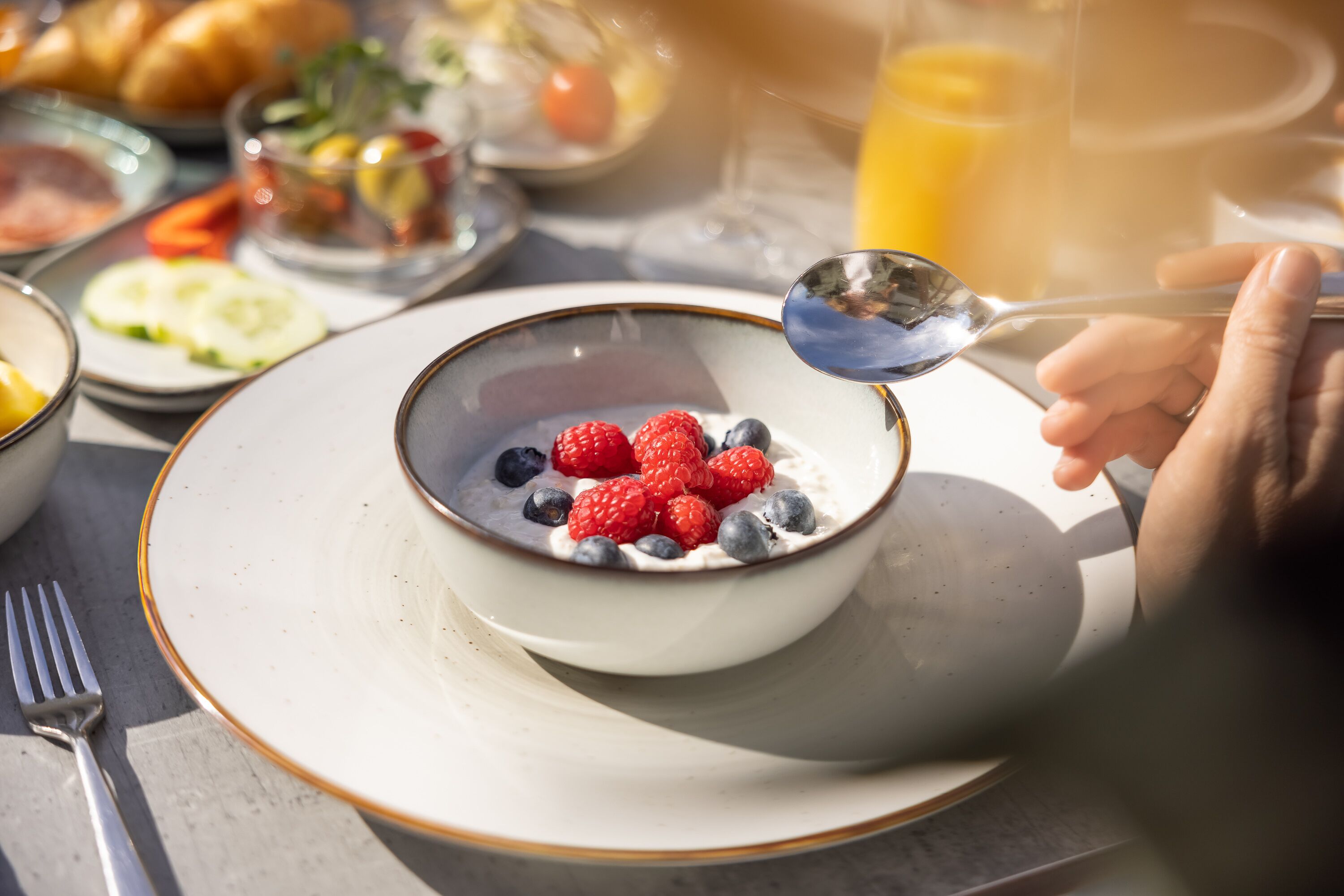 A breakfast setting with a bowl of yogurt topped with berries, a glass of orange juice, and various other breakfast items on the table.