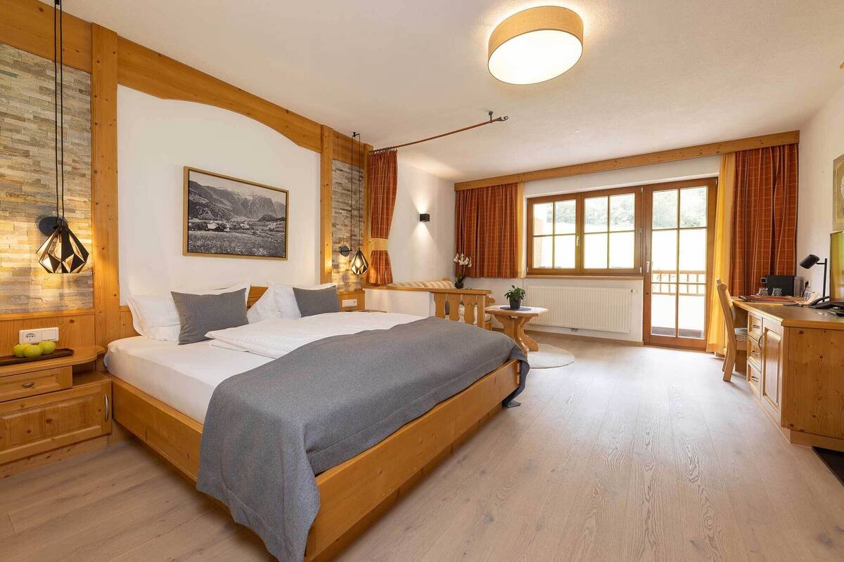 Un dormitorio espacioso con una cama grande, cabecera de madera, una mesita de noche y un ventanal con cortinas que ofrece vistas al exterior.