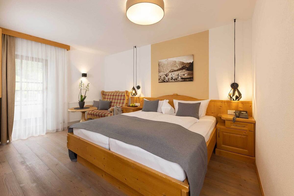 Un dormitorio con una cama grande, mesitas de noche, una lámpara, un cuadro en la pared y una ventana con cortinas.