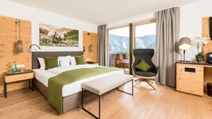 A modern hotel room with a large bed, a desk, a chair, and a view of mountains through the window. - Aktiv Panoramahotel Daniel (Sautens)