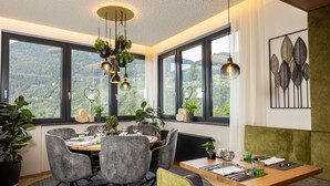 A dining area with a table set for four, surrounded by grey chairs, a wooden table, and a view of a mountainous landscape through large windows. - Aktiv Panoramahotel Daniel (Sautens)