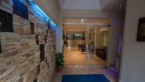 Un pasillo con pared de piedra, alfombra azul y puerta de vidrio que da a una habitación con una silla y una mesa.