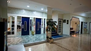 Un hall espacioso con piso de mármol, puertas azules y una escalera que sube a un nivel superior.