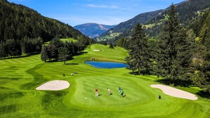 Un parcours de golf avec des bunkers de sable, un étang et des collines boisées en arrière-plan.