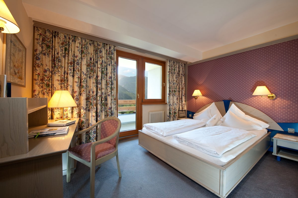 Une chambre d’hôtel équipée d’un lit, d’un bureau, d’une chaise, de lampes et offrant une vue sur l’extérieur.