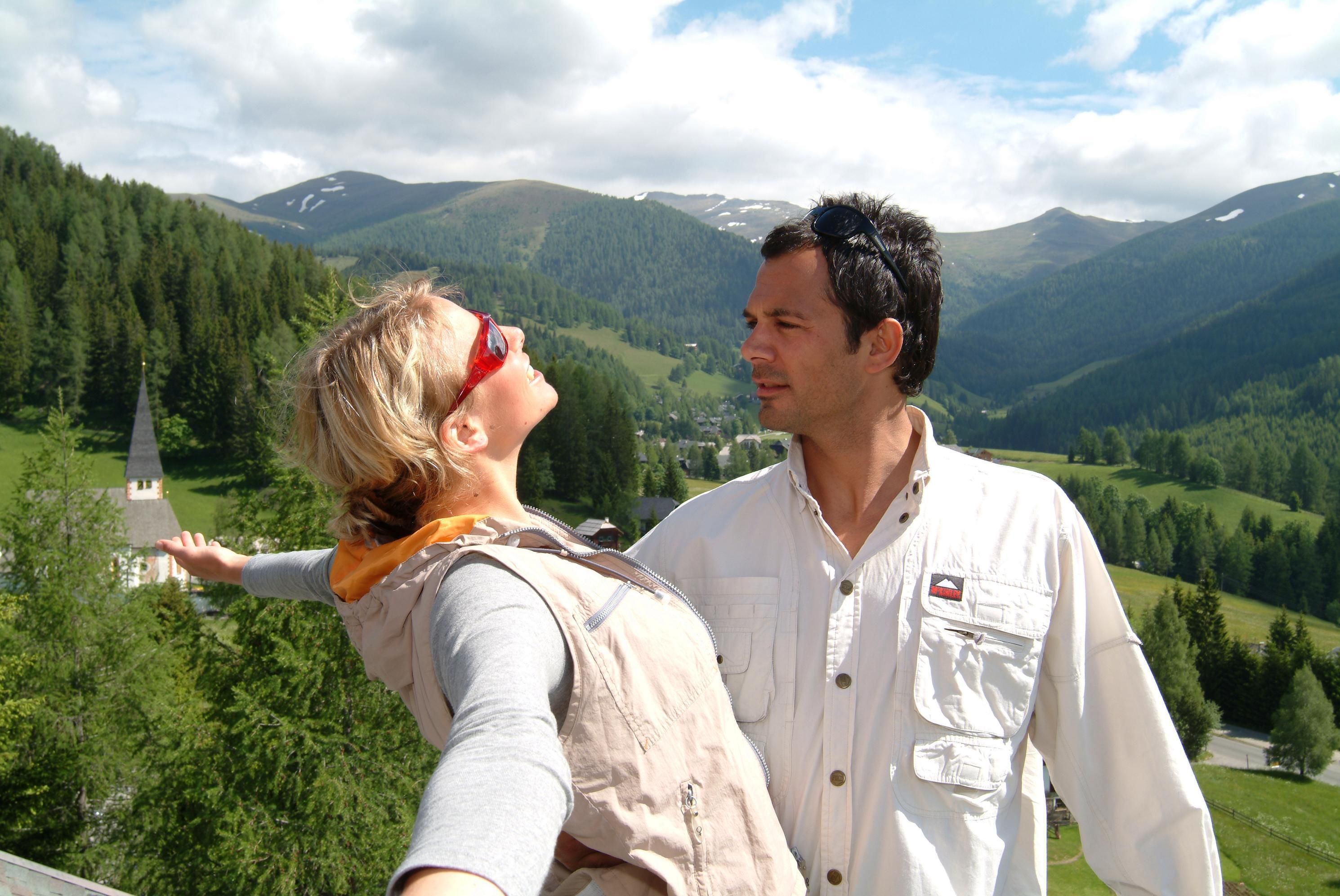 A couple taking a selfie with a scenic mountain view in the background.