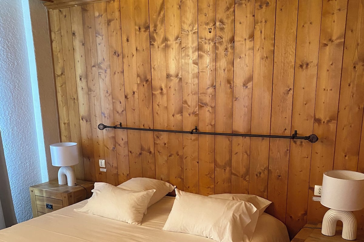 Une chambre à coucher avec une tête de lit en bois, un grand lit recouvert de draps blancs, deux tables de chevet avec des lampes et une commode.