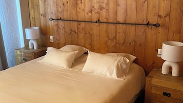 A bedroom with a wooden headboard, a large bed with white linens, two bedside tables with lamps, and a nightstand with drawers.